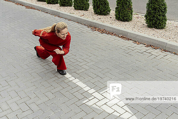 Blond woman with ponytail preparing to run near arrow sign on road