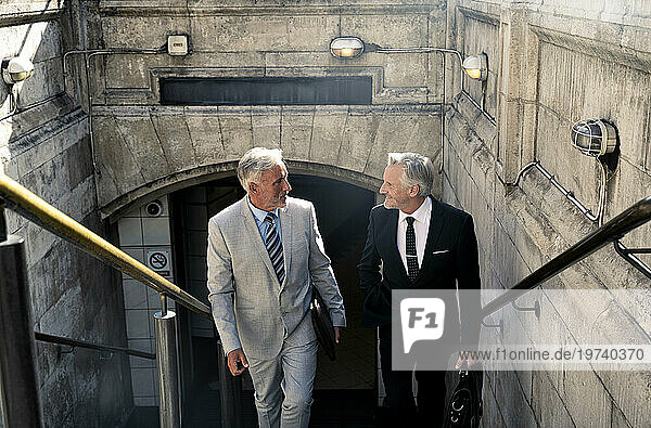 Senior businessman talking to colleague and moving up on staircase