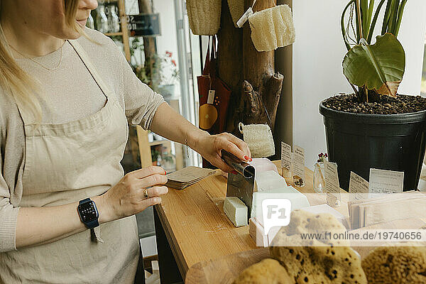Woman cutting bar of soap on table in zero waste store