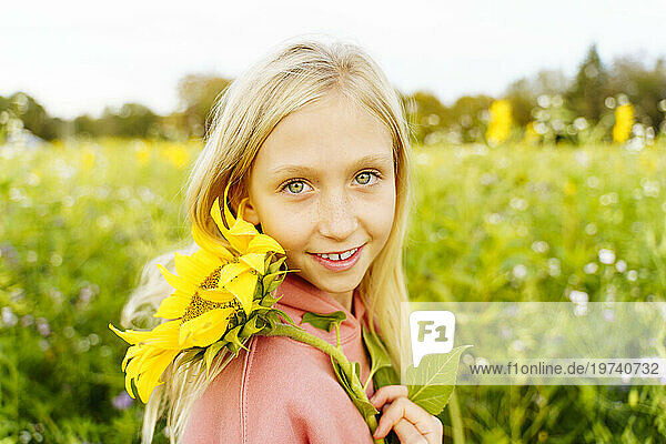 Smiling blond girl holding sunflower in field
