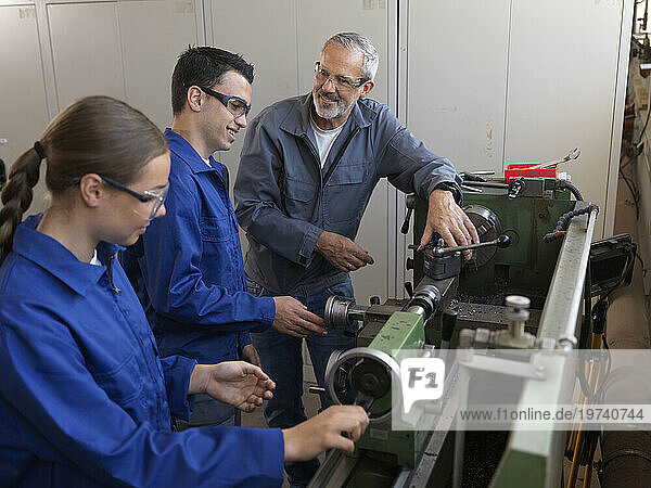 Instructor discussing with trainees over lathe at workshop
