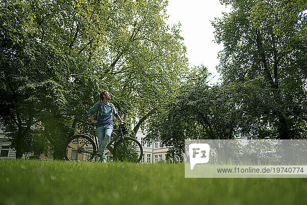 Man leaning on bicycle and looking at trees in park