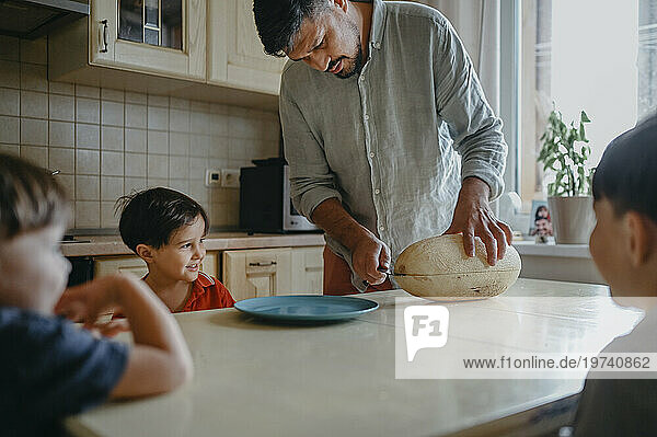 Father cutting melon with children at table in kitchen