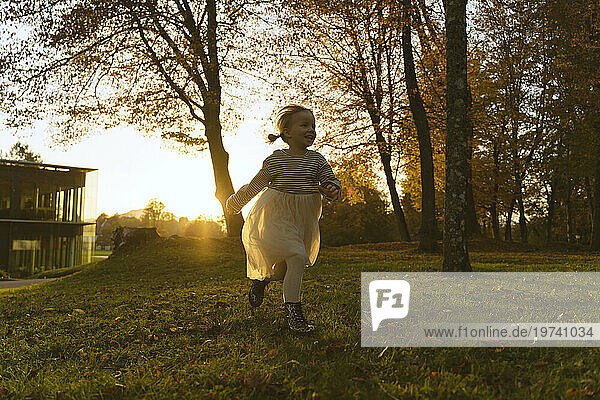 Happy girl running near tree in park at sunset