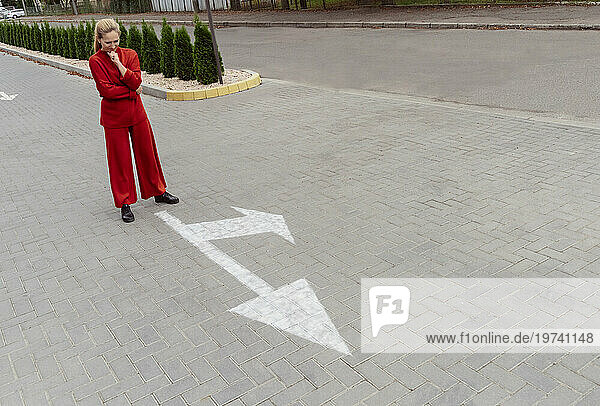 Thoughtful woman with hand on chin standing near arrow sign at street