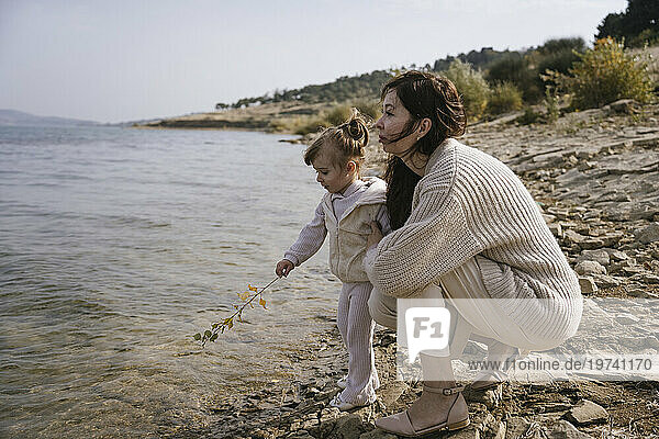 Mother with daughter holding twig near lake