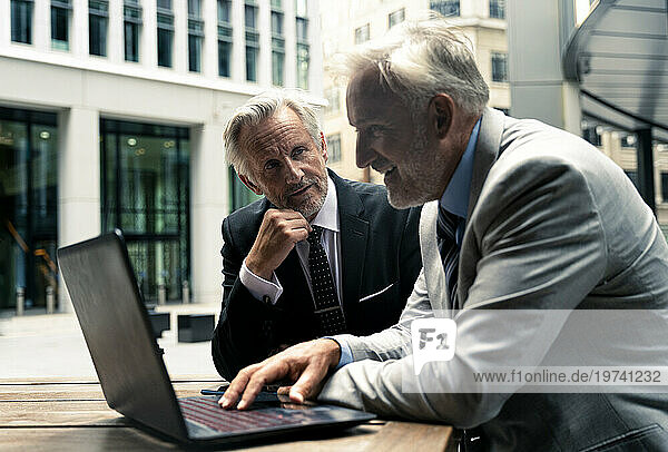 Smiling senior businessman discussing with colleague over laptop at table