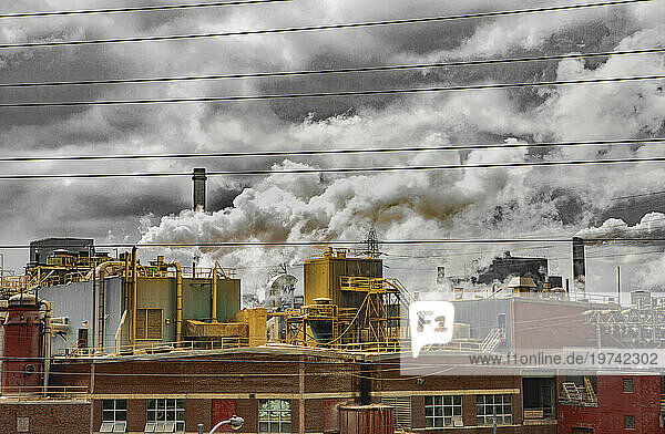 Pulp mill with smoke stacks and billowing emissions into the cloudy sky; St John  New Brunswick  Canada