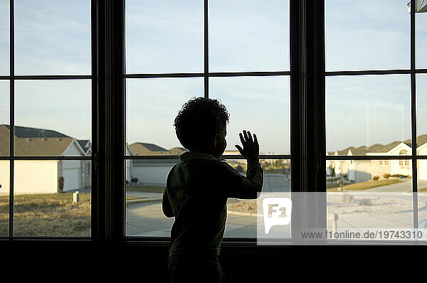 Toddler boy looks out the window of his home to the neighbourhood outside; Lincoln  Nebraska  United States of America
