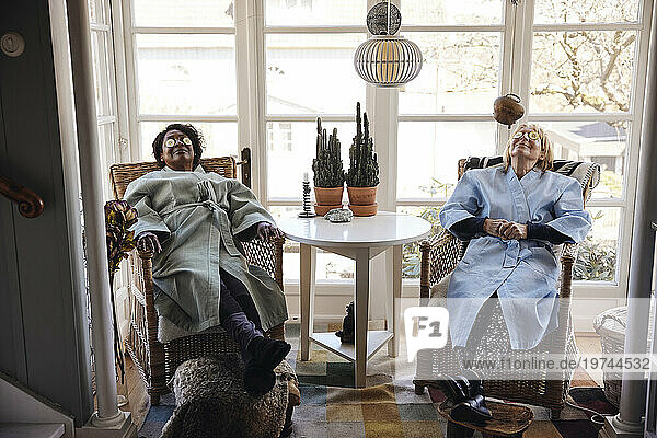 Multiracial female friends with cucumber slices on eyes relaxing together at home