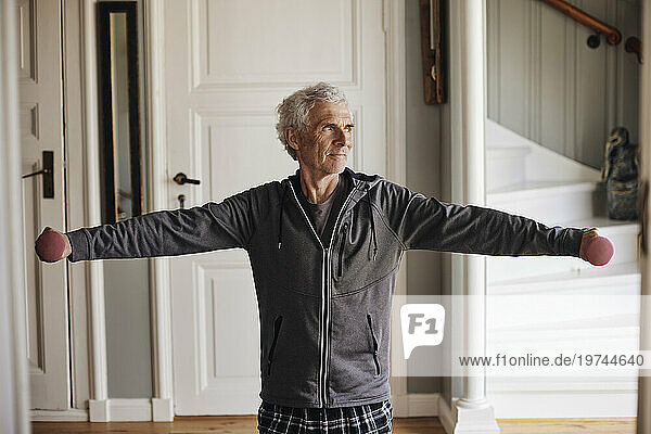 Senior man with arms outstretched exercising with dumbbells at home