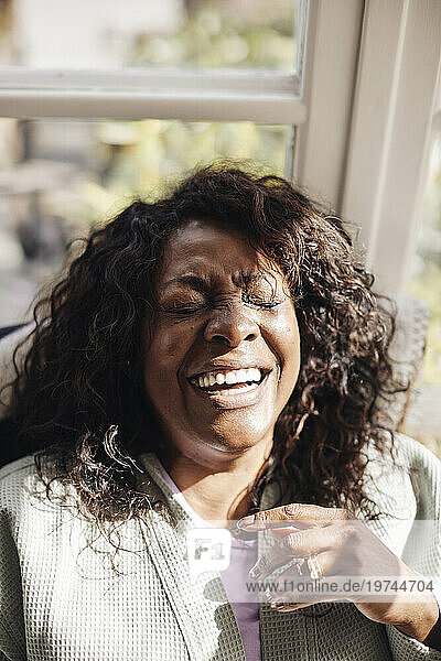 Mature woman with eyes closed laughing in sunlight at home