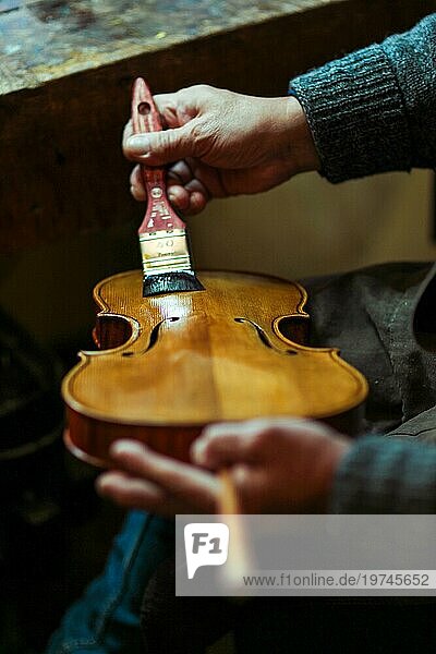 Senior Experte Geigenbauer Geigenbauer  faltige alte Hand Lack mit Pinsel klassische handgemachte Geige malen natürlichen Zutaten Rezept in Cremona Italien Heimat der besten Handwerker dieser Art  Makro Nahaufnahme  selektiven Fokus  Bokeh