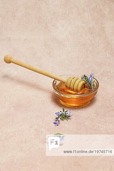 Natürlicher Honig in einer Glasschale mit einem Holzlöffel und frischen Rosmarinzweigen in Blüte