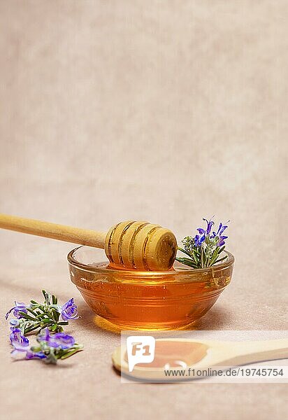 Honig in einer Glasschale mit einem Holzlöffel und frischen Rosmarinzweigen in Blüte
