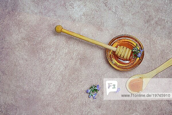 Draufsicht auf natürlichen Rosmarinhonig in einer Glasschale mit einem Holzlöffel und frischen Rosmarinzweigen in Blüte