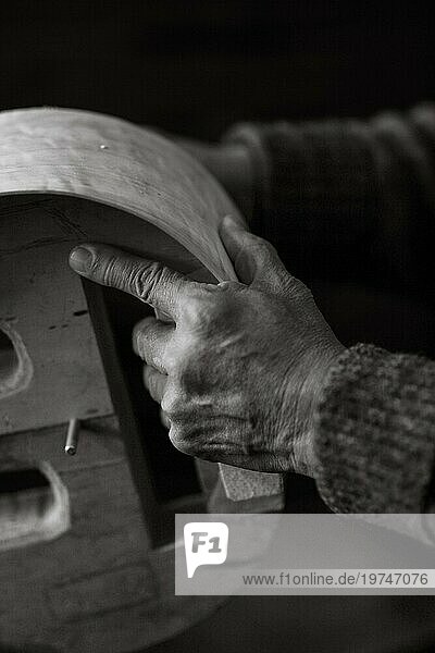 Runzelige Hand von Senior Luthier handwerklichen Geigenbauer schnitzen sculpt Meißel Rippen eines neuen klassischen Modells Cello in der Werkstatt Cremona Italien  schwarz und weiß  selektiver Fokus  Bokeh