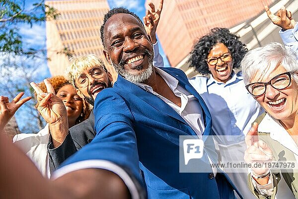 Frontalansicht eines niedlichen eleganten afrikanischen Geschäftsmannes  der ein Selfie mit Mitarbeitern im Freien macht