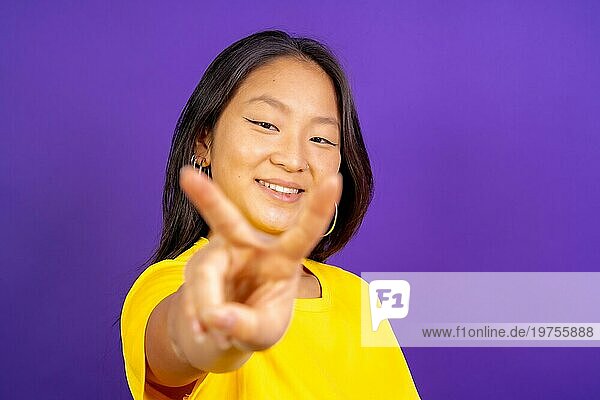 Studio Foto mit lila Hintergrund einer chinesischen Frau gestikulieren Sieg lächelnd in die Kamera