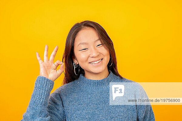 Asiatische Frau  die kühl und wunderbar in die Kamera schaut  auf einem gelben Hintergrund