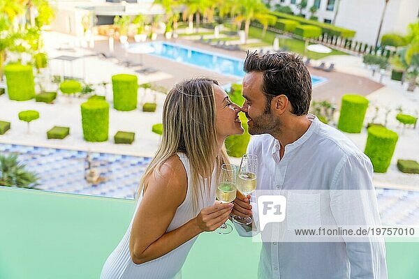 Ein frisch verheiratetes Paar küsst sich  während es mit Champagner auf der Terrasse eines Luxushotels anstößt