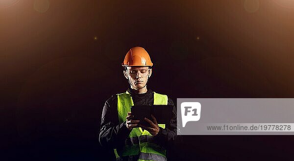 Ingenieurbüro  ein männlicher Bauarbeiter mit Schutzhelm auf dunklem Hintergrund verwendet ein Tablet. Geschäftsprozessmanagement und Bauinspektor mit BIM Technologie in einem Bauprojekt