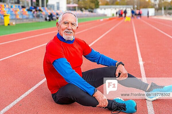 Porträt eines lächelnden  sportlichen alten Mannes  der nach einem Lauf müde auf einer Bahn sitzt