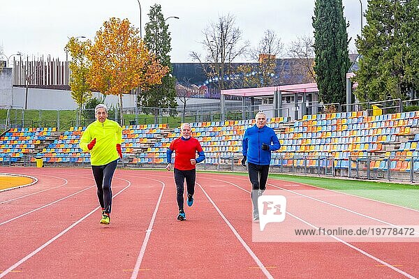 Frontalansicht von drei reifen  sportlichen Männern  die auf einer Leichtathletikbahn laufen