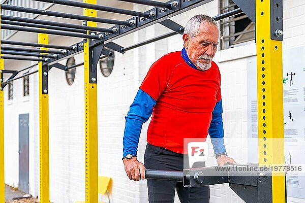 Älterer Mann im Ruhestand mit sportlicher Winterkleidung beim Training auf einem öffentlichen Sportplatz