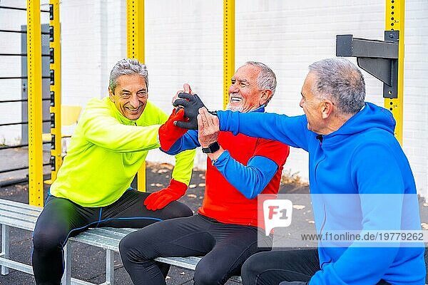Drei ältere Männer im Ruhestand geben sich auf einem Sportplatz im Freien die Hand