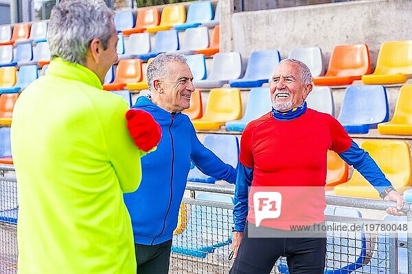 Lächelnde alte Sportfreunde wärmen sich auf einer Wiese auf  bevor sie gemeinsam loslaufen