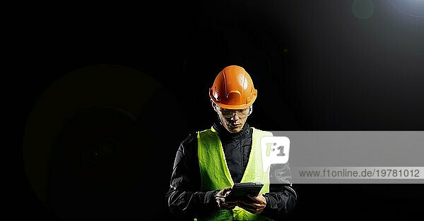 Ingenieurbüro  ein männlicher Bauarbeiter mit Schutzhelm auf dunklem Hintergrund verwendet ein Tablet. Geschäftsprozessmanagement und Bauinspektor mit BIM Technologie in einem Bauprojekt