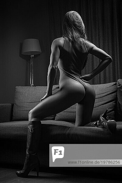 Sexy Model mit perfekter Figur posiert im Bodysuit auf der Couch. Gemischte Medien
