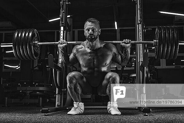 Bild eines kraftvollen Athleten hockt mit einer Langhantel in einem Fitnessstudio. Fitness und Bodybuilding Konzept. Gemischte Medien