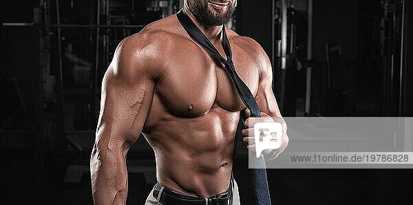 Attraktiver Mann mit Krawatte posiert in der Turnhalle. Business und Bodybuilding Konzept. Sportliche Aktivitäten. Gemischte Medien