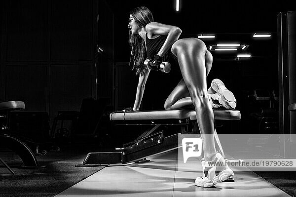 Große sportliche Frau führt eine Übung auf einer Bank in einem Fitnessstudio mit einer Hantel durch. Ansicht von hinten. Fitness und Bodybuilding Konzept. Gemischte Medien