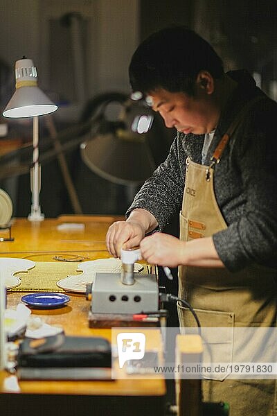 Asiatischer Geigenbaumeister und Kunsthandwerker bei der Herstellung von Biegekontrollstreifen in einem Eisenwerkzeug für eine neue rohe Boden und Vorderplatte einer klassischen handgefertigten Geige in seiner Werkstatt in Cremona  Italien  Europa