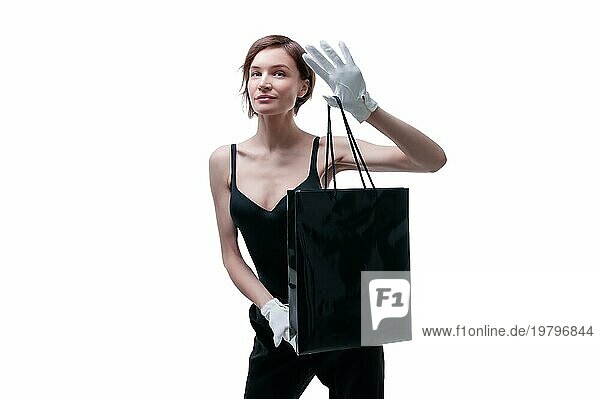 Schöne junge Frau in weißen Handschuhen hält eine schwarze Basteltasche in der Hand. Konzept der Shopaholics. Ausgeben. Geschenke für die Feiertage. Schwarzer Freitag. Einkaufszentren. Gemischte Medien