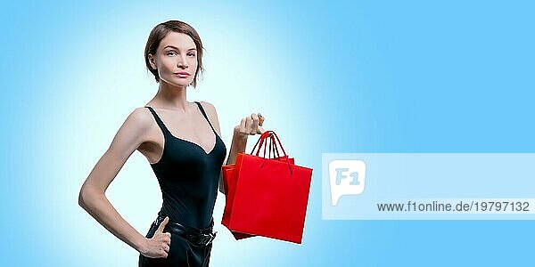 Schöne junge Frau hält ein rotes Paket in ihrer Hand. Shopaholics Konzept. Ausgeben. Geschenke für die Feiertage. Schwarzer Freitag. Einkaufszentren. Gemischte Medien