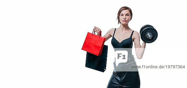 Schöne schlanke Frau posiert im Studio mit einer Hantel und Geschenktüten. Geschenk Konzept. Mitgliedschaft im Fitnessstudio