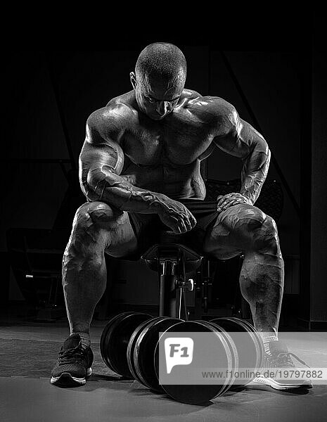 Muskulöser Mann sitzt auf einer Bank neben riesigen Hanteln. Bodybuilding und Kraftdreikampf Konzept.