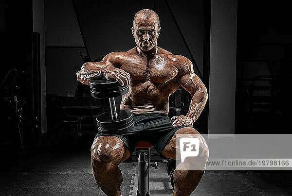 Muskulöser Mann sitzt auf einer Bank mit Hanteln. Bodybuilding und Kraftdreikampf Konzept.