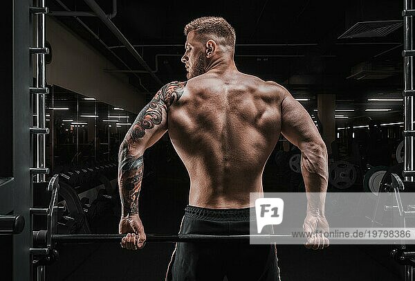 Porträt eines Sportlers  der auf einer Langhantel im Fitnessstudio sitzt. Blick von hinten. Konzept für Bodybuilding und Fitness.