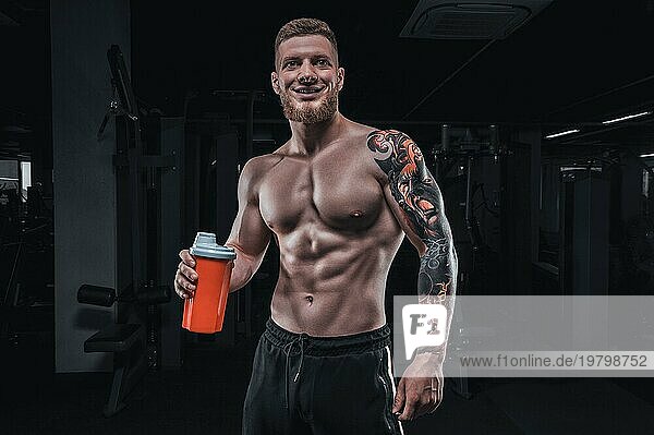 Porträt eines Sportlers  der mit einem Shaker im Fitnessstudio steht. Bodybuilding und Fitness Konzept.