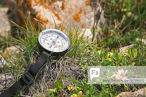 Ein Magnetkompass liegt auf einem Stein neben dem Gras