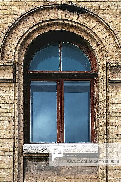 Vintage gewölbtes Fenster in der Wand aus gelbem Backstein. Schwarzes Glas in einem kastanienbraunen dunkelroten Holzrahmen. Das Konzept der antiken Vintage Architektur in Gebäudeelemente