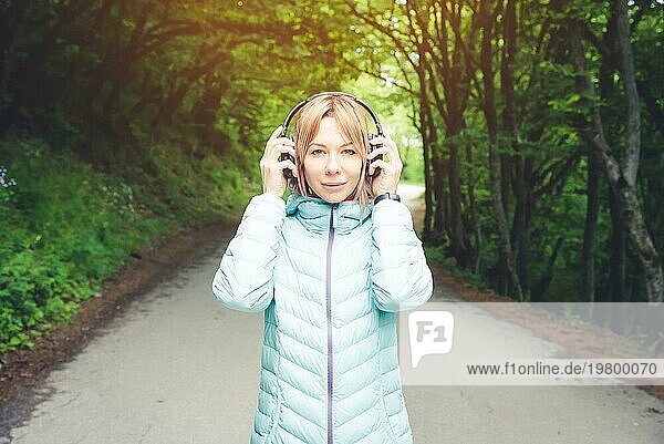 Porträt einer schönen jungen Frau mit Kopfhörern  die draußen im Wald Musik hört. Fröhliche Musik
