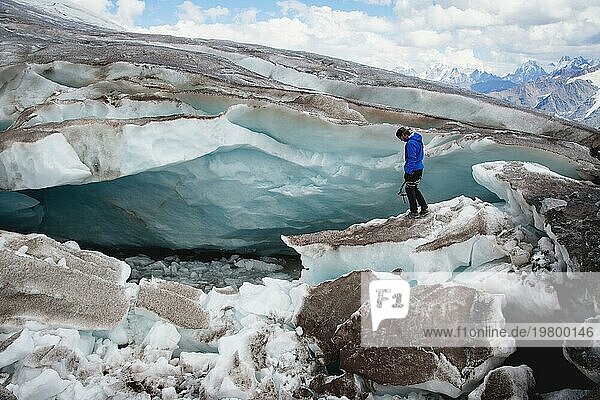 Der Reisende mit Mütze und Sonnenbrille steht in den verschneiten Bergen auf dem Gletscher. Reisender in einer natürlichen Umgebung