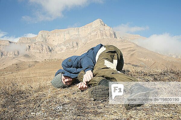 Ein Tourist mit Hut und Bart liegt auf dem Boden und fühlt sich in den Bergen schlecht. Eine Person  die das Bewußtsein verloren hat. Gefahr Unfallkonzept