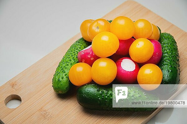 Ganze frische Gemüsesalatzutaten liegen auf einem Holzbrett auf dem Küchentisch. Leckere und gesunde pflanzliche Lebensmittel